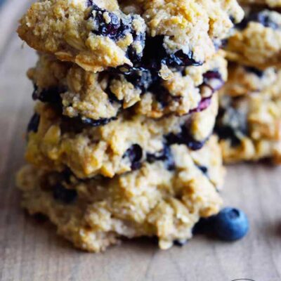 A stack of four blueberry breakfast cookies on a cutting board. You can see blueberries throughout the cookies.