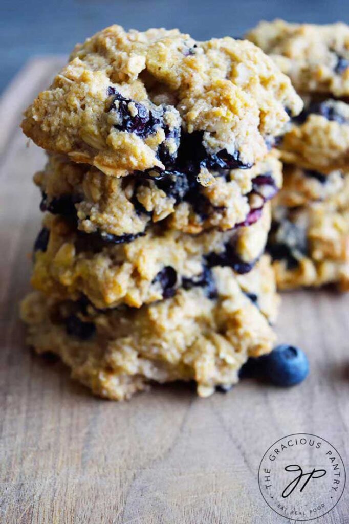 A stack of four blueberry breakfast cookies on a cutting board. You can see blueberries throughout the cookies.