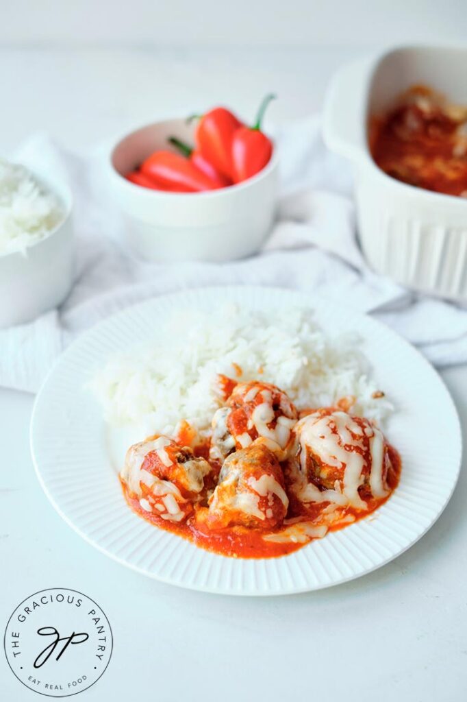 Cheesy Baked Meatballs plated with rice on a white plate in front of the casserole dish they were baked in.