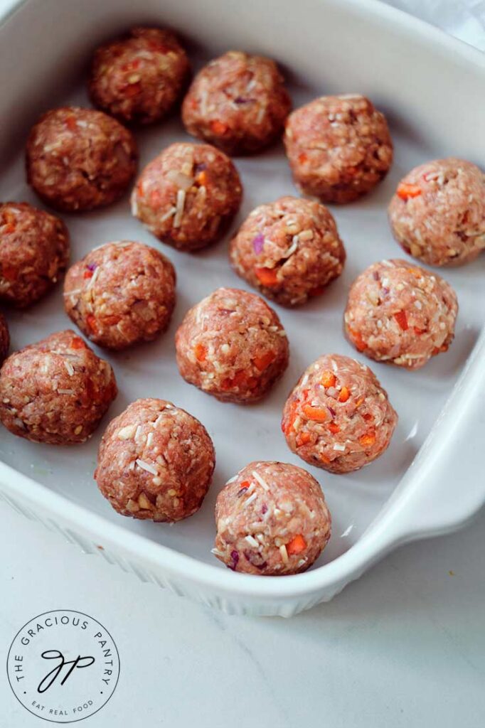 Just made, uncooked meatballs sitting in a white casserole dish waiting for sauce and cheese before baking.