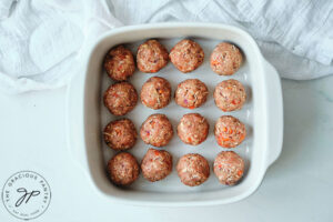 An overhead view looking down into a white casserole dish filled with raw meatballs, waiting to be topped and baked.