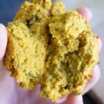 A hand holding a drop biscuit, broken in half to show the inside.