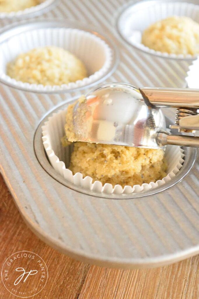 Muffin dough being scooped into the muffin liners in the muffin pan.