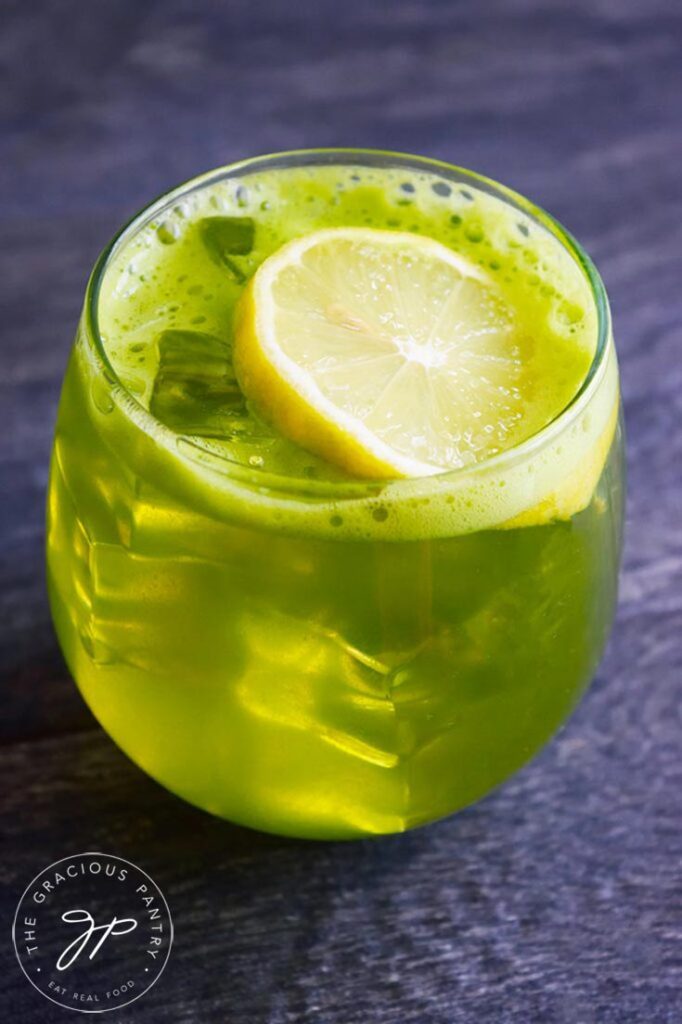 Green Lemonade in a stemless wine glass with a lemon slice resting on the ice.