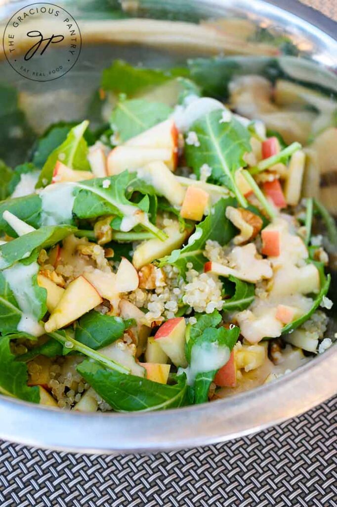 A side view of this Kale Quinoa Salad in a mixing bowl with dressing on it.