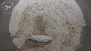 Stirring the dough with a wooden spoon until it becomes thick enough to knead by hand.