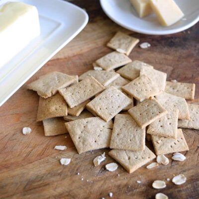 Oat crackers on a cutting boar with a butter dish and a cheese dish sitting behind them.