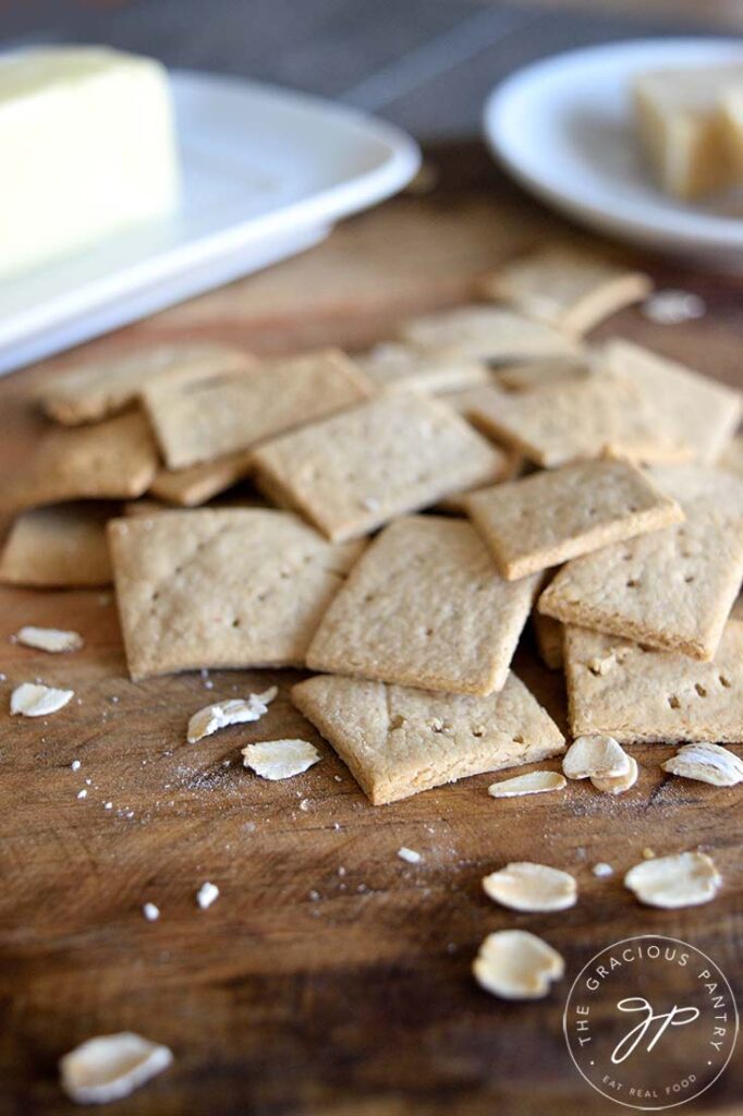 A pile of oat crackers sit with a butter dish just behind them on the counter.