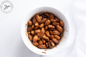 Mixing the almonds and spices together with the oil in a small, white mixing bowl.