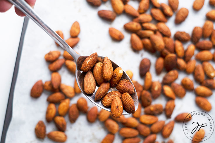 The finished, roasted almonds, just out of the oven. A spoon holds a few of them close to the camera.