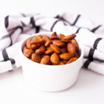 Spicy Roasted Almonds in a small white serving bowl with a kitchen towel laying just behind the bowl.