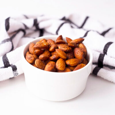 Spicy Roasted Almonds in a small white serving bowl with a kitchen towel laying just behind the bowl.