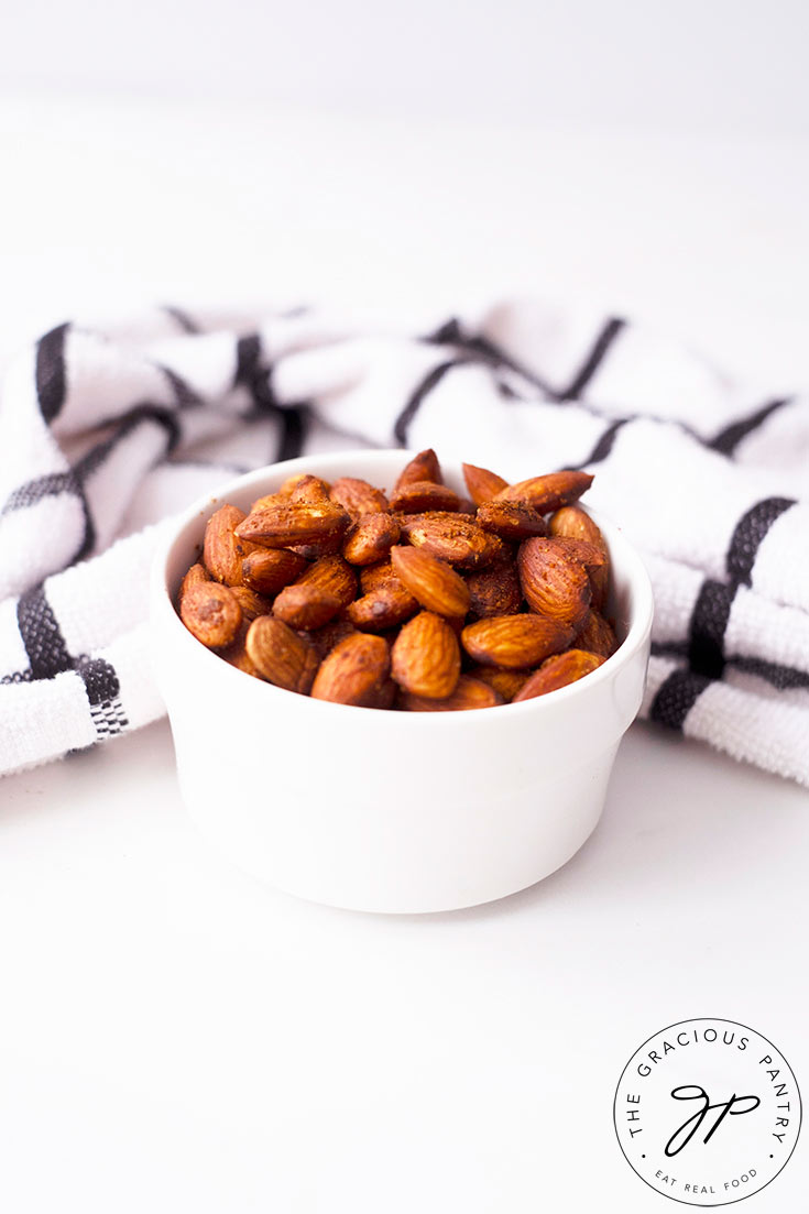 Spicy Roasted Almonds in a small white serving bowl with a kitchen towel laying just behind the bowl.