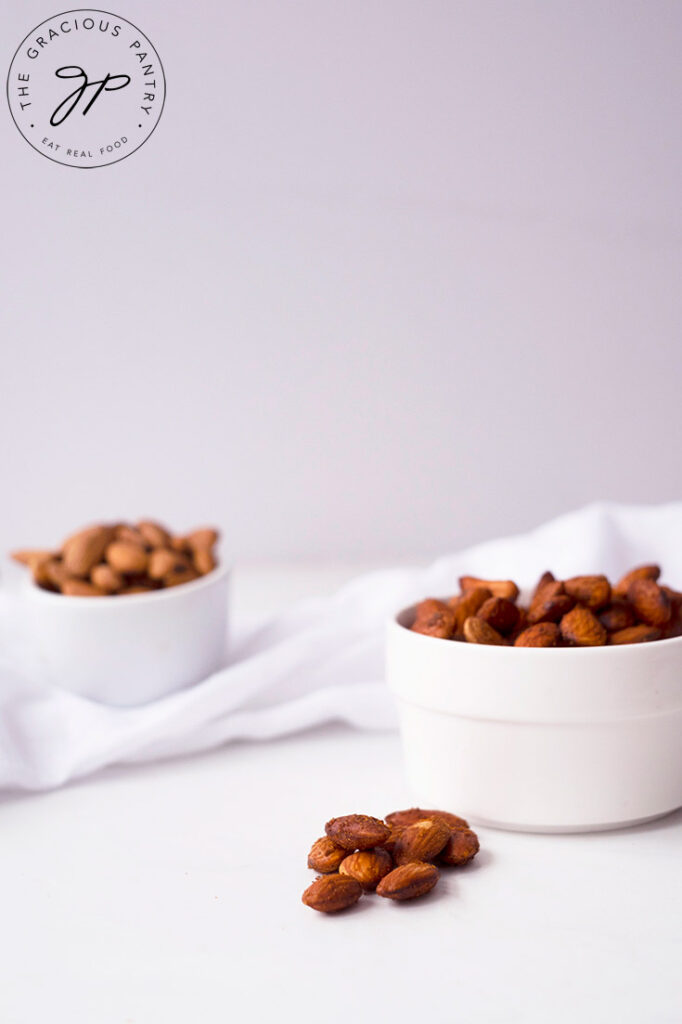 A side view of two small, white bowl sitting on a white background, filled with Spicy Roasted Almonds.