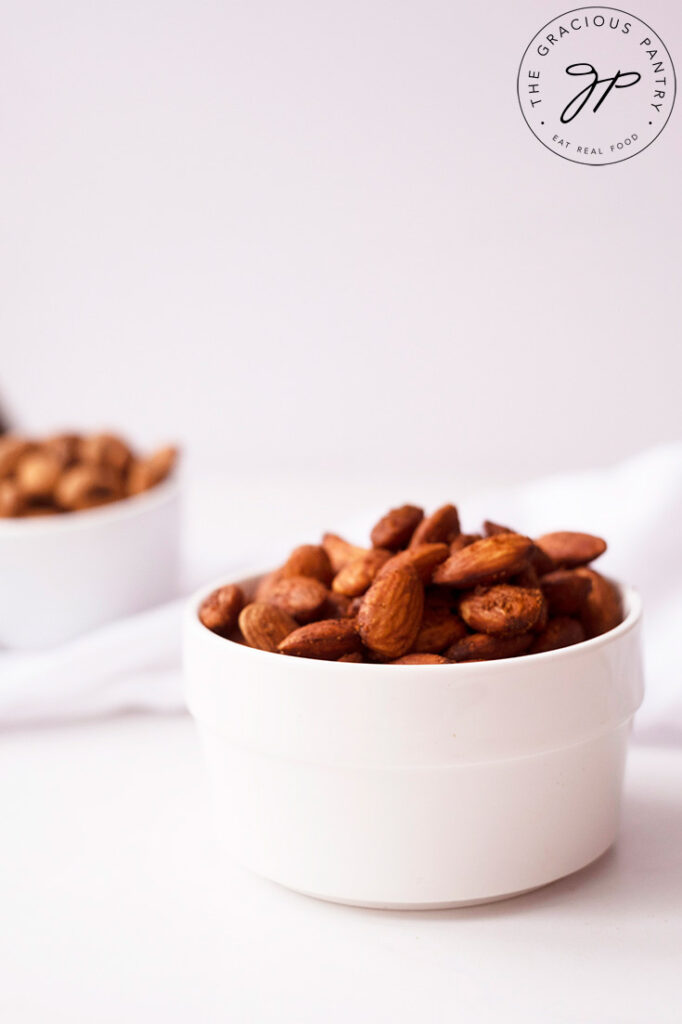 An up close side view of a small white bowl filled with Spicy Roasted Almonds.