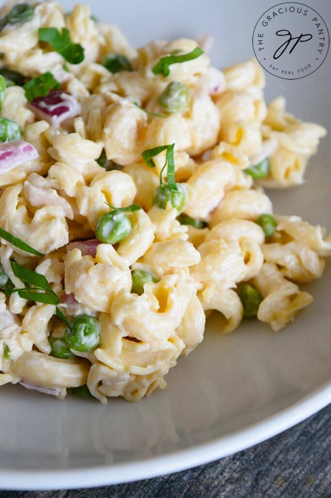 And up close view of this Tuna Pasta Salad Recipe in a white bowl. You can see the cavatappi pasta, green peas and bits of purple onion in the noodles.