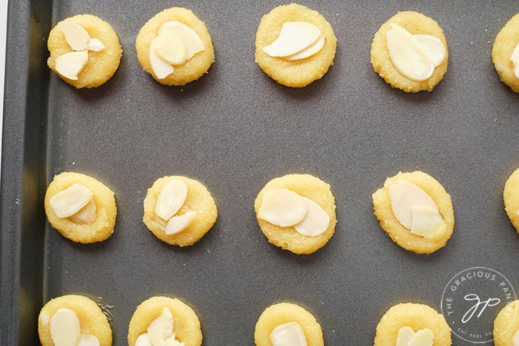 Almond cookies lined up on a cookie sheet, ready to go into the oven for baking.