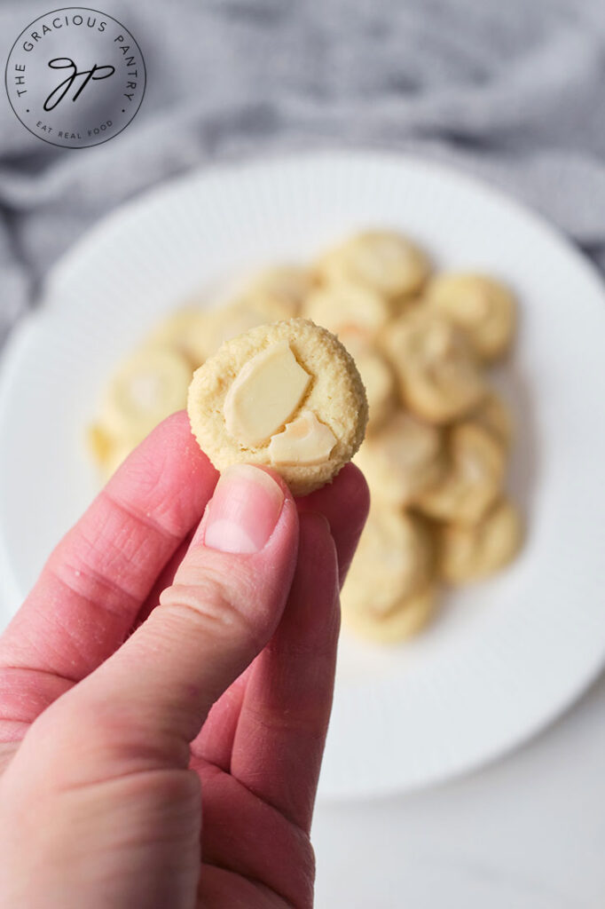 A hand holding a single Almond Cookie over a plated filled with Almond Cookies.