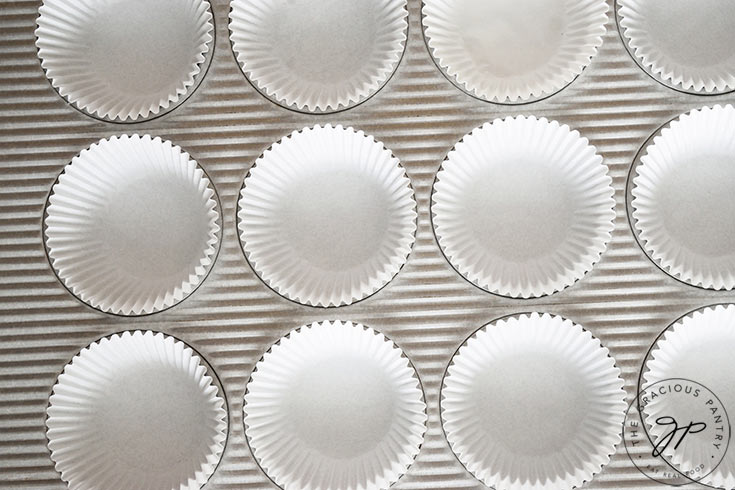 A muffin pan with white cupcake liners.