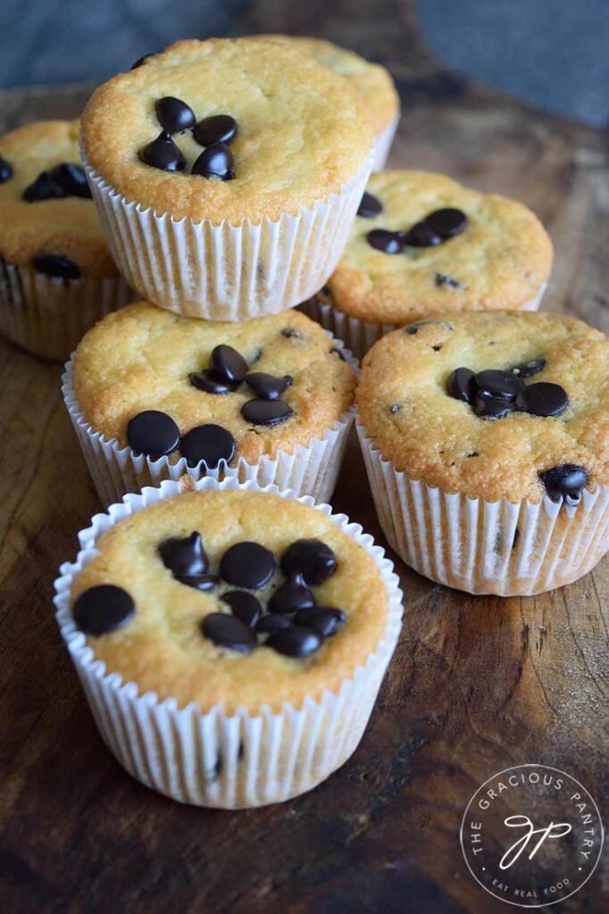 A stack of almond flour muffins sitting on a wooden surface. Chocolate chips are baked into the tops of the muffins.