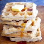 A stack of Almond Flour Waffles with a pat of butter on top and some maple syrup being poured over the top.