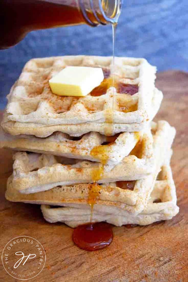 A stack of Almond Flour Waffles with a pat of butter on top and some maple syrup being poured over the top.