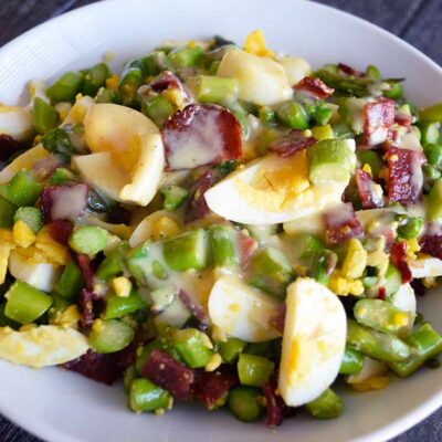 Asparagus Salad served in a white bowl with vinaigrette over the top.