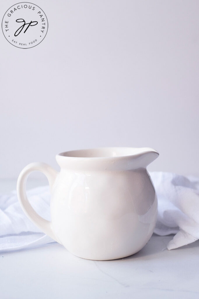 A white pitcher sits on a white background, ready to be filled with the finished Chicken Broth Gravy Recipe.