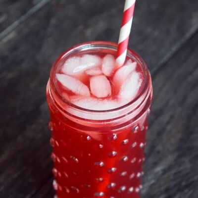 The finished Hibiscus Lemonade in a glass cup with a red and white straw.