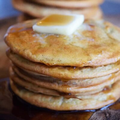 A stack of Leftover Oatmeal Pancakes with a pat of butter on top and maple syrup drizzled over the top.