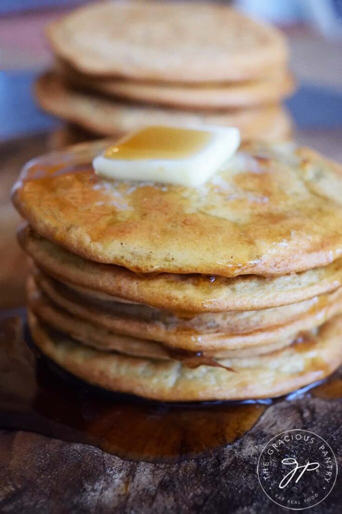 A stack of Leftover Oatmeal Pancakes with a pat of butter on top and maple syrup drizzled over the top.