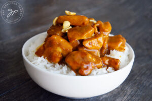 Peanut butter chicken in a white bowl in a bed of rice.