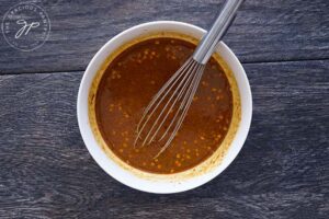 Peanut butter sauce in a white bowl with a whisk resting on the side.