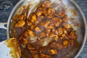 Peanut sauce poured over chicken chunks in a skillet.