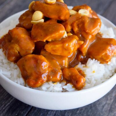 Peanut butter chicken in a white bowl in a bed of rice.