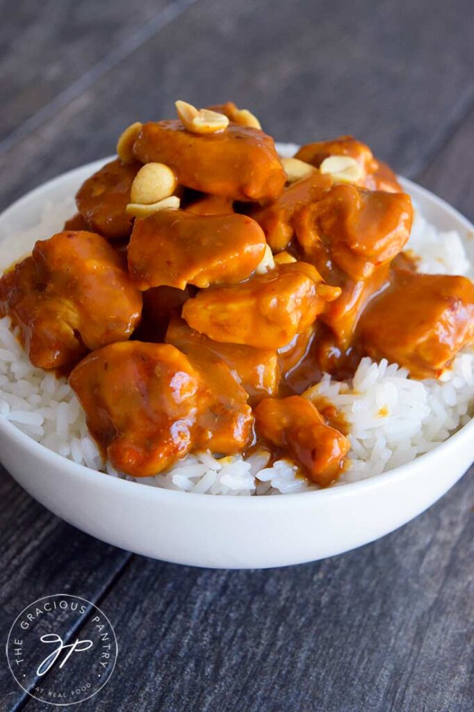 A front view of Peanut butter chicken in a white bowl in a bed of rice.