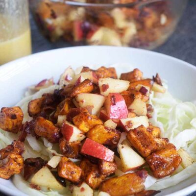 A side view of the served Roasted Potato Salad on a bed of cabbage. Dressing sits to the side.