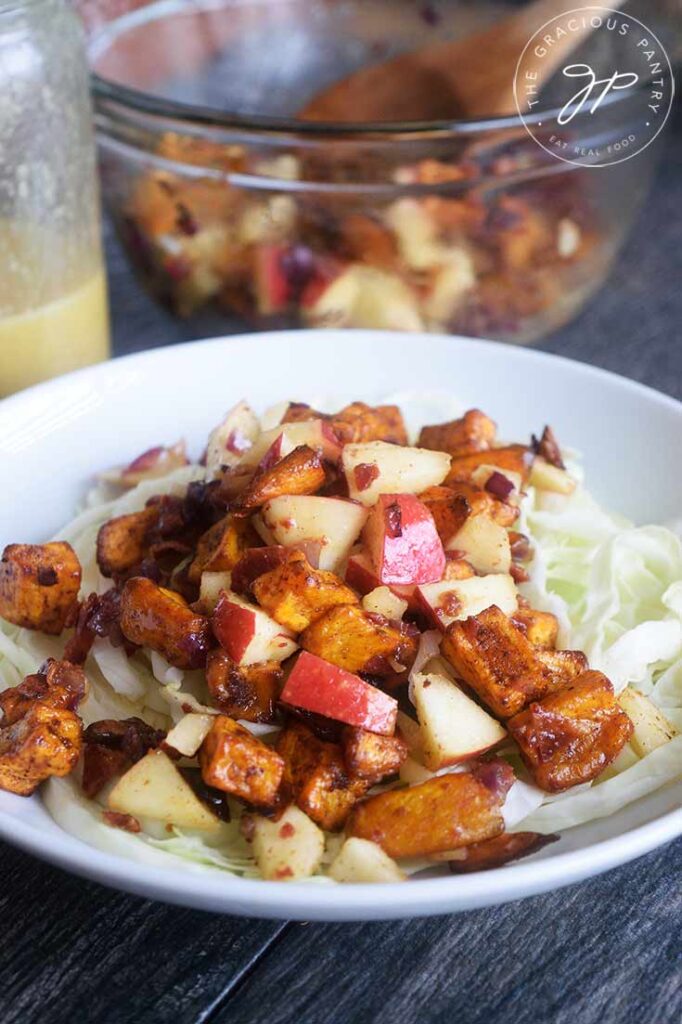 A side view of the served Roasted Potato Salad on a bed of cabbage. Dressing sits to the side.