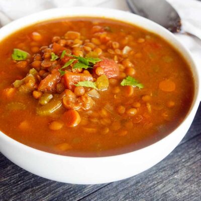 The finished Slow Cooker Curry Lentil Soup in a white bowl. A spoon rests on the table to the right of the bowl.