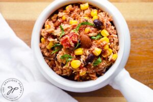 The finished Slow Cooker Southwestern Chicken served in a white crock. A white towel lays to the side of the bowl.