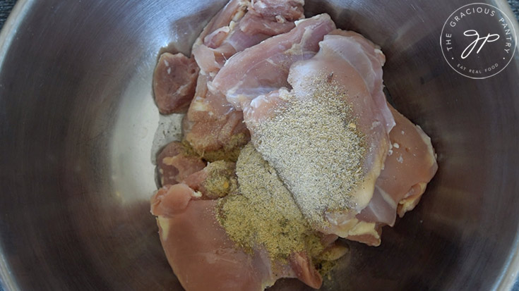 The chicken thighs in a mixing bowl with the oil and spices.