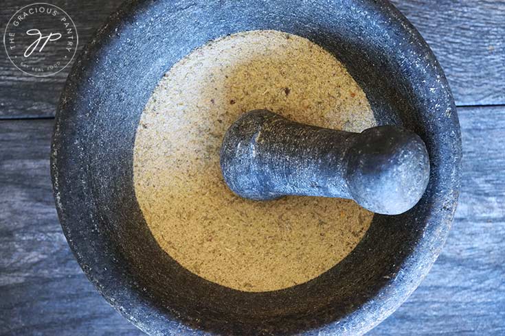 And overhead view looking down into a mortar filled with Tuscan Seasoning. The pestle rests on the side of the mortar.