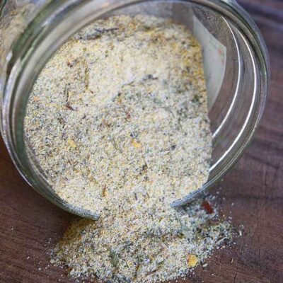 The finished Tuscan Seasoning in a jar, tipped on its side so the seasoning spills out onto a wooden surface.