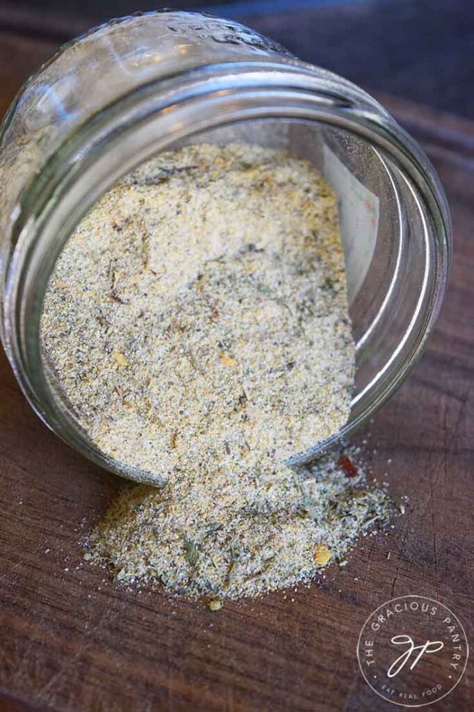The finished Tuscan Seasoning in a jar, tipped on its side so the seasoning spills out onto a wooden surface.