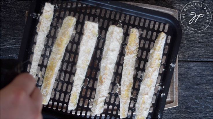 Placing the breaded Cajun Zucchini Sticks on an air fryer tray for air frying.