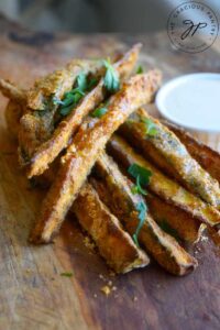 Cajun Zucchini Sticks piled on a cutting board with a small dish of dip next to them.