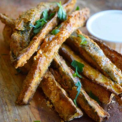 Cajun Zucchini Sticks piled on a cutting board with a small dish of dip next to them.