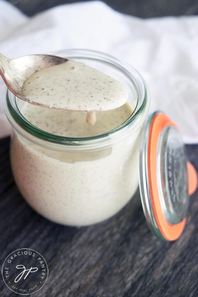 A spoon holds up a spoonful of Dairy Free Ranch Dressing over the jar it's stored in.