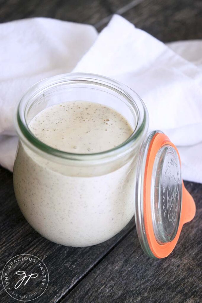 A glass jar filled with Dairy Free Ranch Dressing sits open with it's lid propped up on the side of the jar.