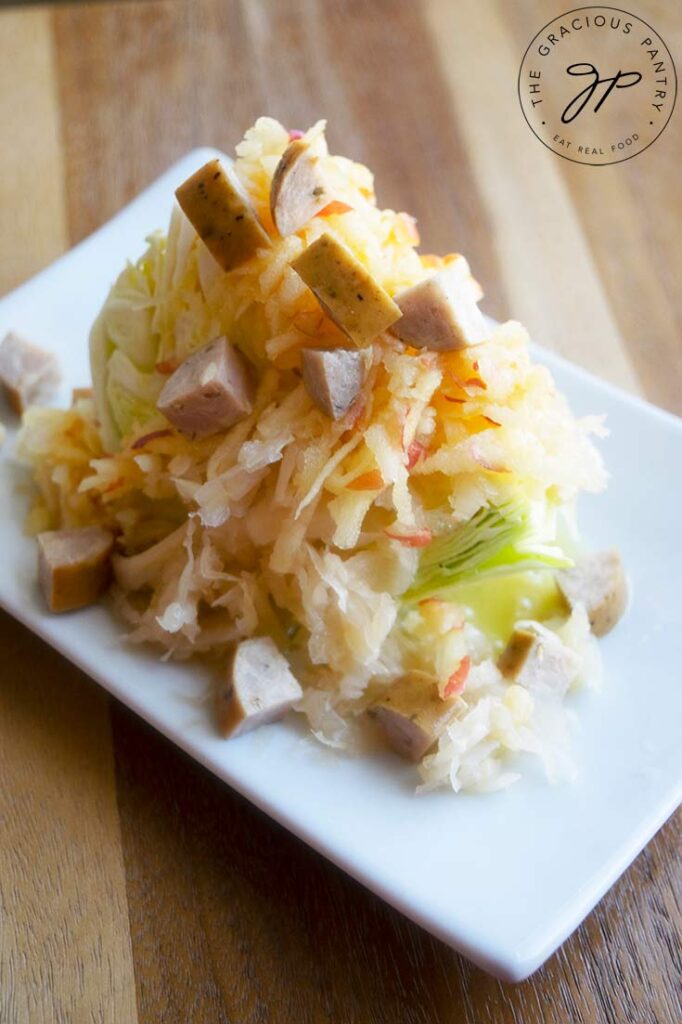 A German wedge salad topped with sauerkraut, shredded apple, chopped sausage and dressing.